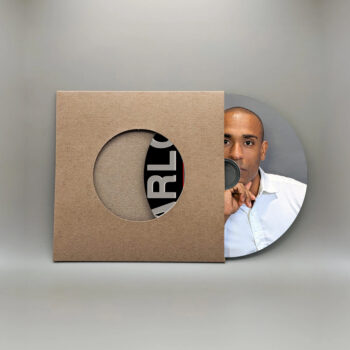 Creative album cover featuring Carlos Simpson, founder of Carlos Simpson Design Studio™, partially hidden behind a vinyl disc. The disc emerges from a brown cardboard sleeve with a circular cutout, revealing the bold typography of “CARLOS SIMPSON.” The photo merges design, branding, and identity through minimalist aesthetics.