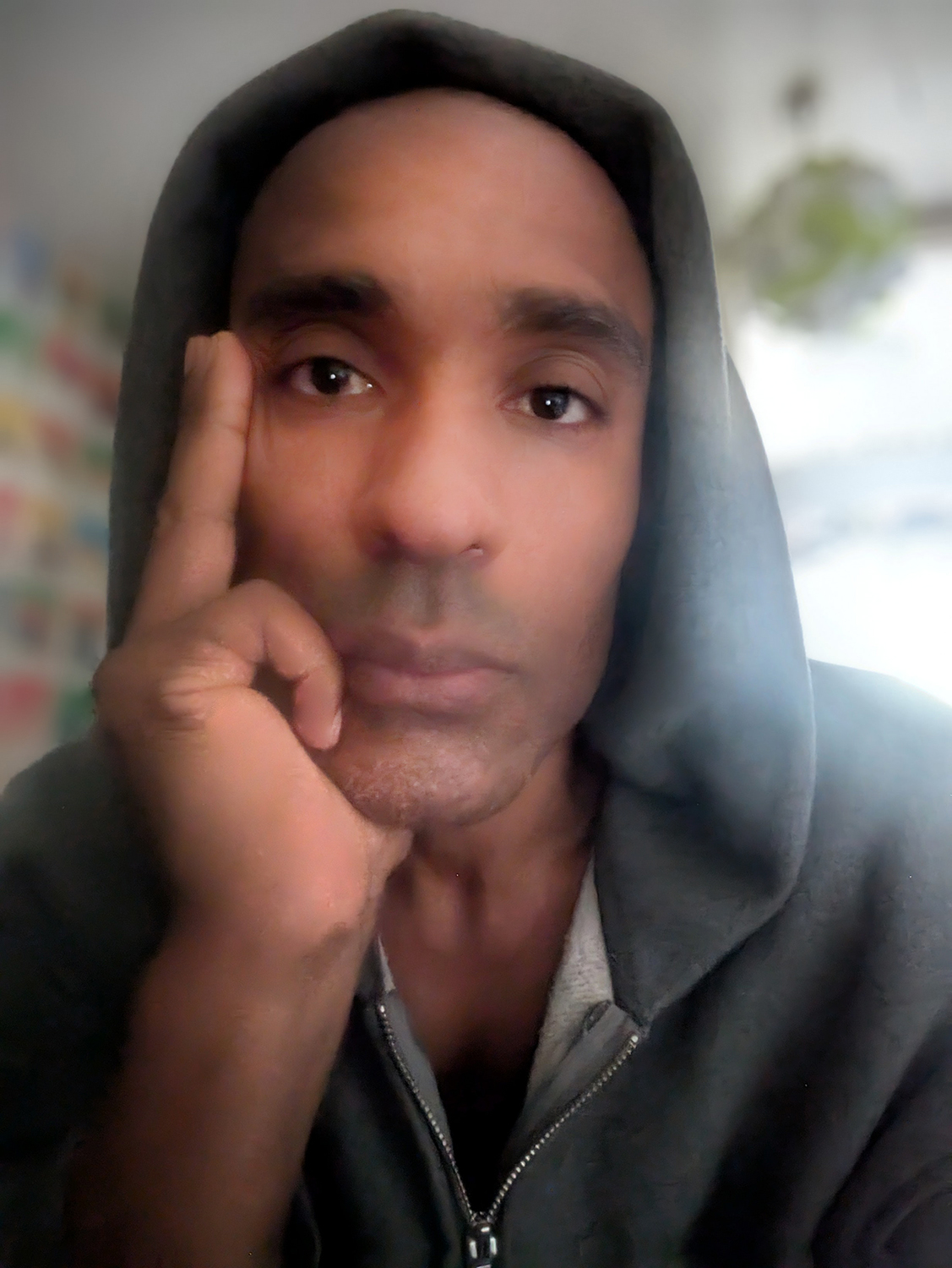 Portrait of Carlos Simpson, London-based artist, designer, and musician, wearing a grey hoodie, looking directly at the viewer.